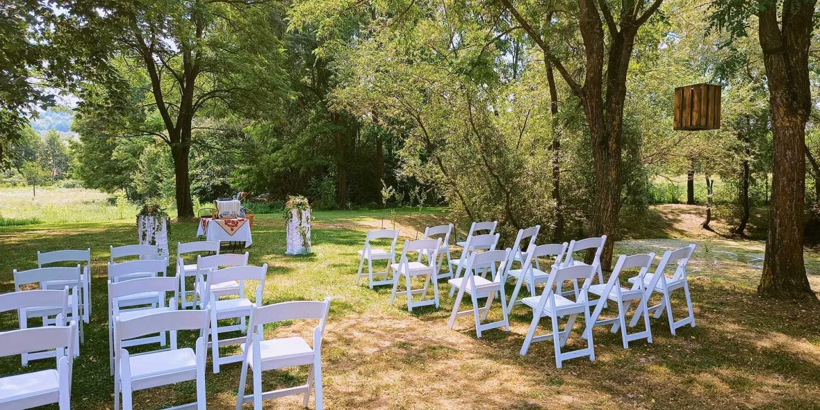 logistica-evenimente-de-inchiriat Vedem locatia unei ceremonii in aer liber cu scaune able inchiriate frumos aranjate. În prim-plan se vede o leagăn.